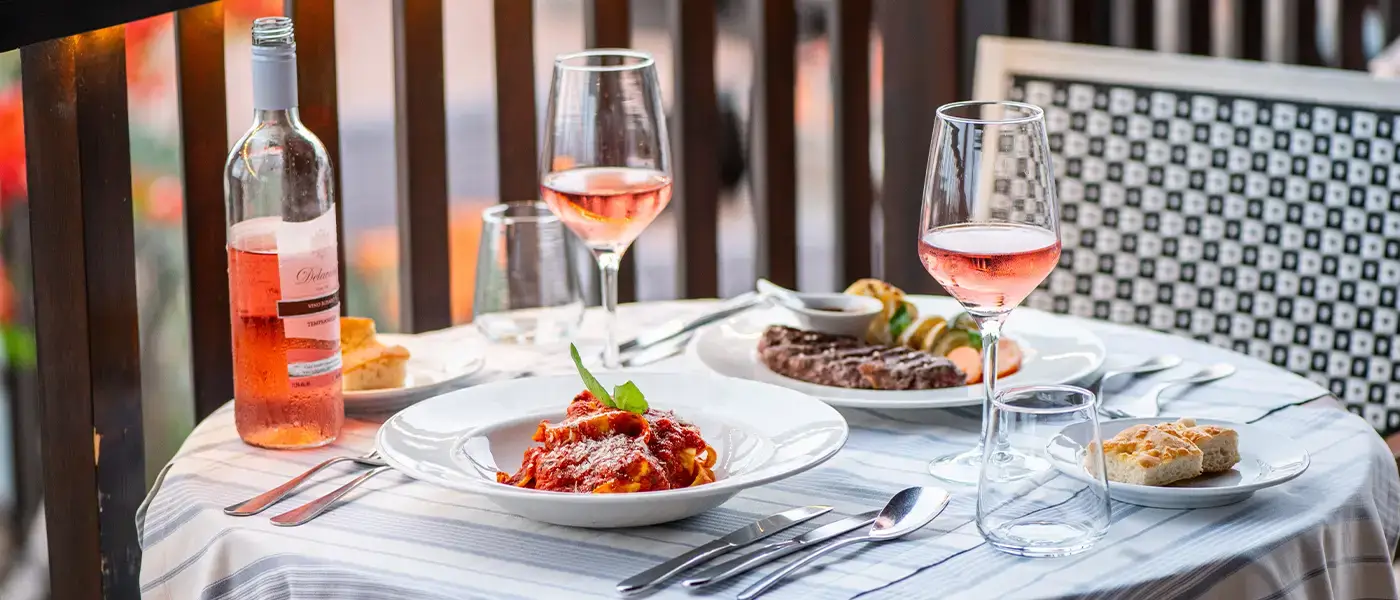 A table laid with pasta, meat and rosé wine